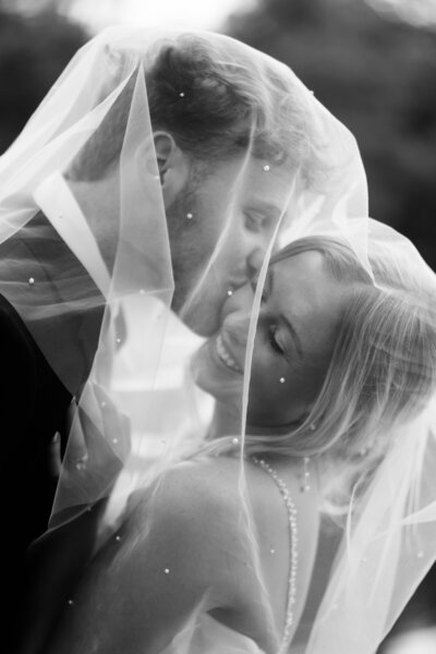 Bride and groom under a veil, he's kissing her cheek