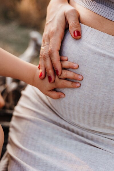 Close Up von Babybauch mit Händen der Mutter und des Geschwisterkinds