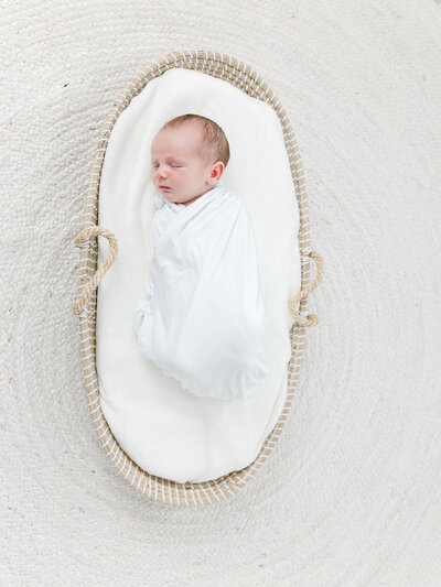 Newborn baby in bassinet swaddled for newborn photography session