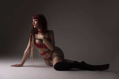girl in red boudoir clothing bra and underwear with red hair posed sittting down on grey backdrop near seattle