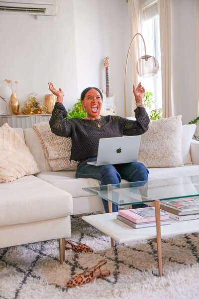 jacinta-gandy-smiling-and-raising-hands-while-working-on-laptop-in-modern-living-room-01