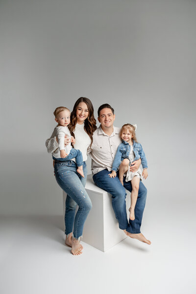 Family in a minimalist studio, parents with two young children in denim and neutral tones. Photographed by Yucaipa family photographer Kaitlyn Dawn Photography.