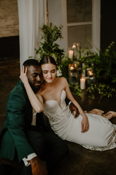 couple sitting on ground for intimate portrait surrounded by candles and greenery