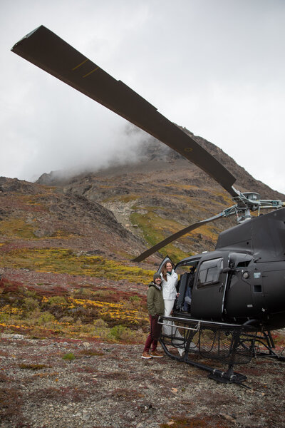 A bride and groom stand outside of the door to a helicopter during their Alaska elopement.