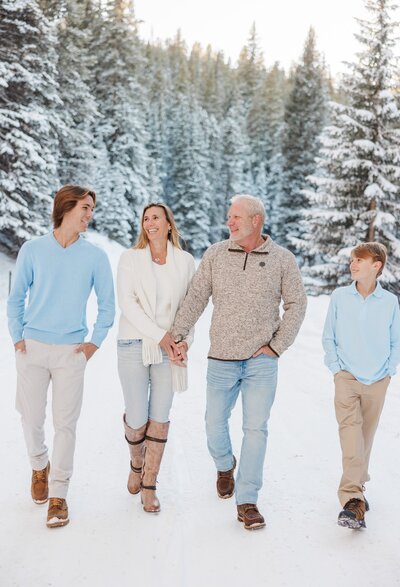 A mom and dad stand in a snow covered mountain in blue and white smiling for their Breckenridge Family Photographer