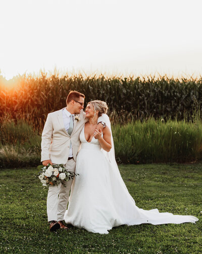 A groom and his bride walk in a field at sunset on their wedding day.