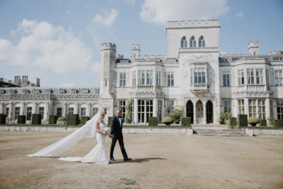 Danielle Armstrong and Tommy Edney walking outside a luxury castle in the UK. Bride wearing a Berta dress, holding a bouquet.