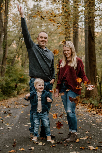 Mom and dad throwing leaves in the air with their young son at Patapsco State Park in Ellicot City Maryland