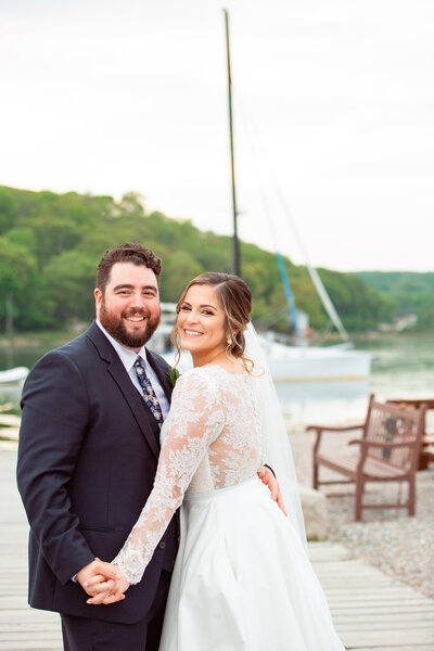 Bride and groom laugh as a sailboat passes behind them during their wedding at the Mystic Seaport.