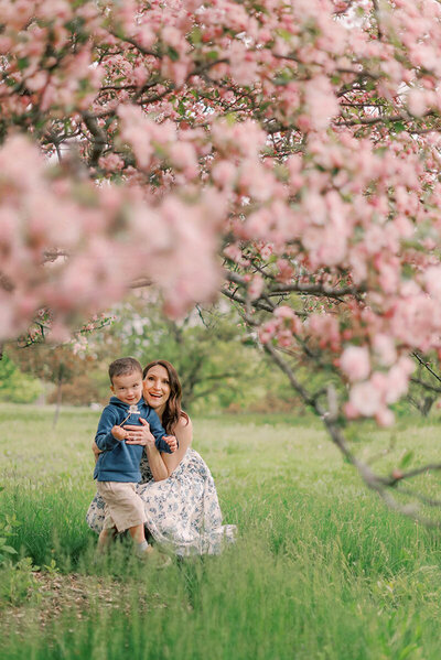 Mom in a white floral dress hugging her young son underneath a pink blossoming tree for her Chicago family pictures
