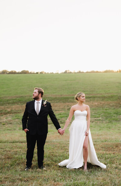 Virginia wedding photographer captures bride and groom holdin ghands and looking off to the side away from each other in a field with a hills behind them for a fall wedding