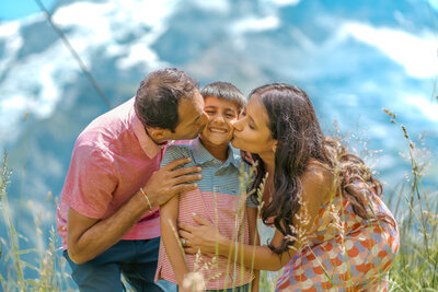 In der bezaubernden Umgebung von Lauterbrunnen zeigen die Eltern ihre Liebe, indem sie ihrem Sohn einen zärtlichen Kuss auf die Wange geben. Ein Moment reiner Zuneigung und Verbundenheit.