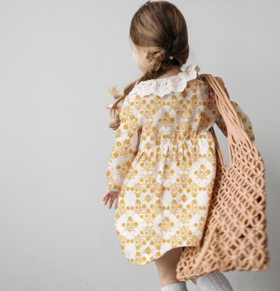 Little girl wears a mustard yellow and white lace collared linen dress with a symmetrical pattern of vintage hand drawn flowers in the style of grandmillennial, French country, vintage modern