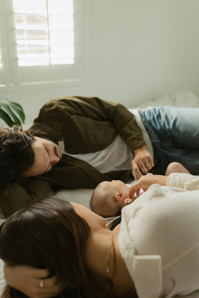 family of 3 laying on bed together
