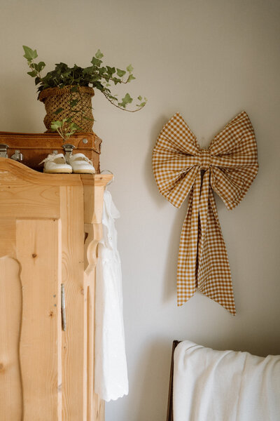 Detail van de babykamer met houten kast en strik aan de muur – warme, persoonlijke elementen vastgelegd in interieurfotografie