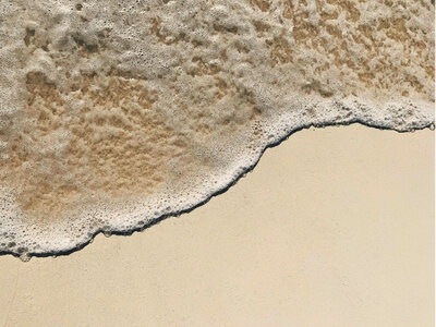 White sand beach with gentle turquoise waves rolling onto the shore. Tailored Oasis Travel Co.