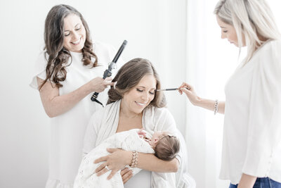 Woman holding baby while getting makeup and hair done