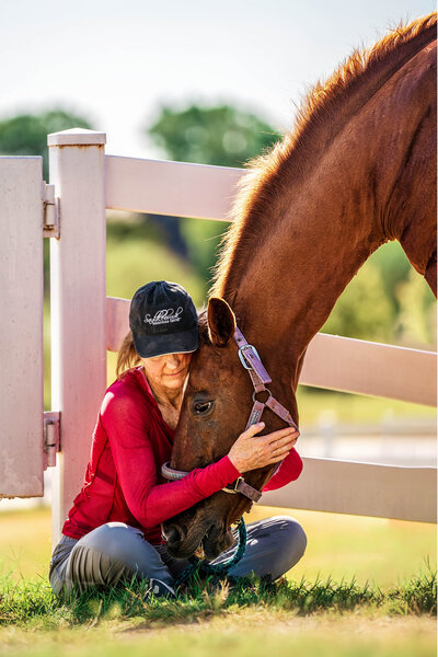 Woman sits on the ground hugging her horse's head in an end of life pet portrait.