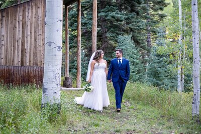 Bride and groom walking in aspen trees holding hands