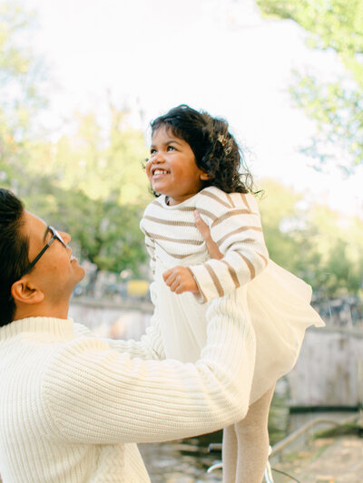 Father throws toddler into the air on the Amsterdam canals at sunset.