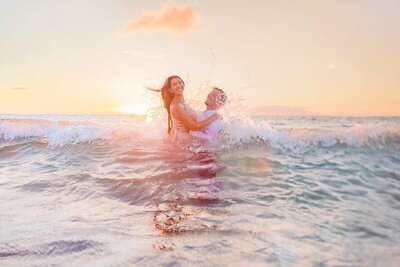 young couple splashes in the water together at sunrise during their engagement photoshoot in Maui