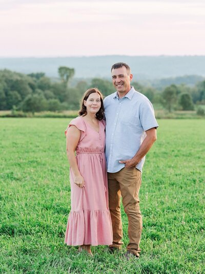Husband and wife standing close with their arms around each other outdoors in a field at sunset for couple’s portraits.