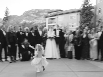 Blurry black and white image of a little girl running towards the bride and groom posing with their family