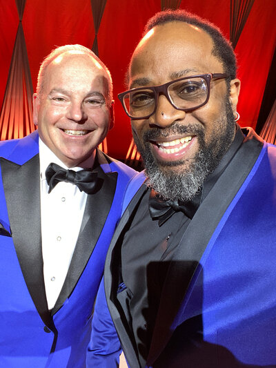 Two men in blue tuxedos smiling for selfie