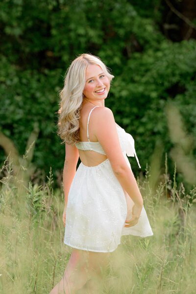 Marvin Ridge High School senior wearing a white dress poses in a Lancaster, SC field wearing a white dress and her hair falling in gentle curls behind her