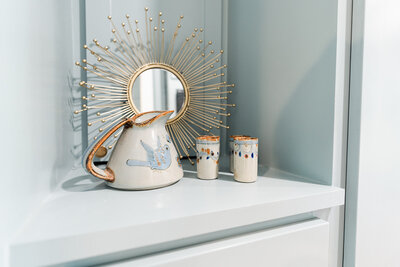 gold starburst  mirror resting on shelf with potter pitcher and cups