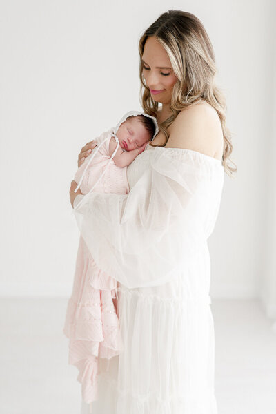 Mother holds newborn baby in bonnet and pink blanket