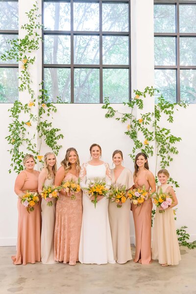 The bride smiles at the camera with her bridesmaids after her wedding at the Distillery in Raleigh.