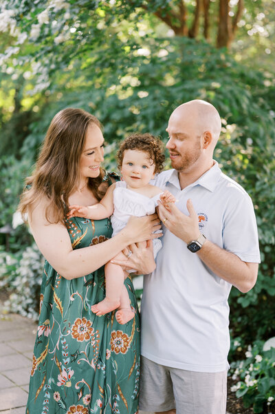 Mom and dad hold baby boy with curly auburn hair  for family photo in Raleigh North Carolina