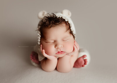 newborn baby smiling for her photo session in Oswego, ny wearing a bear bonnet in tan white