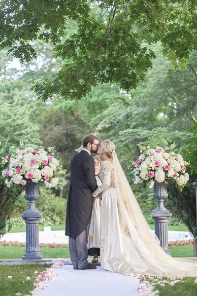 Bride and groom kissing outside between two large flower arrangements