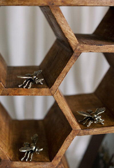 Wooden hexagonal shelves with small decorative metallic bees placed in some compartments. White background.