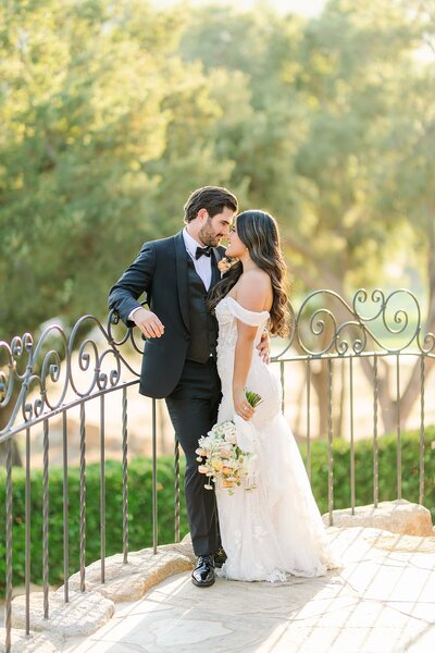 Bride and groom pose for portraits at Mt. Woodson Castle in San Diego. The bride wears a beautiful white gown, while the groom is dressed in a classic black suit, with the historic castle and lush greenery in the background.