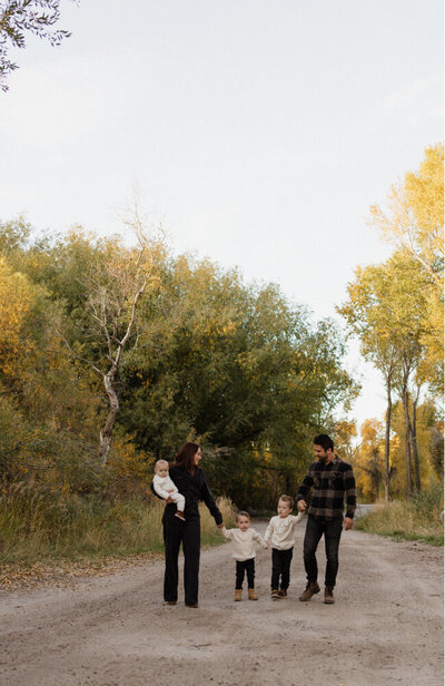 A family of a husband, wife, and 3 children all holding hands and smiling at each other.