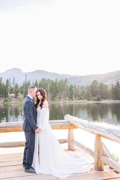 Groom nuzzling in on bride standing on the dock over the water in RMNP, Colorado