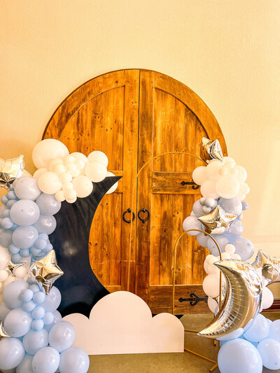 light blue and white bealoon decor with metalic silver boon and starts around a large moon and cloud cutout, infront of a double wood arched door