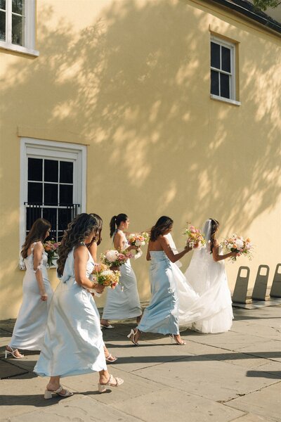 A group of bridesmaids in colorful dresses walk behind the bride holding their pastel colored bouquet 