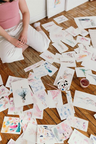 Watercolor artwork spread across wooden floor, showcasing Stephanie Anne's creative process in Montreal