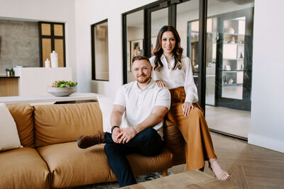 husband and wife sitting on tan couch in marketing office