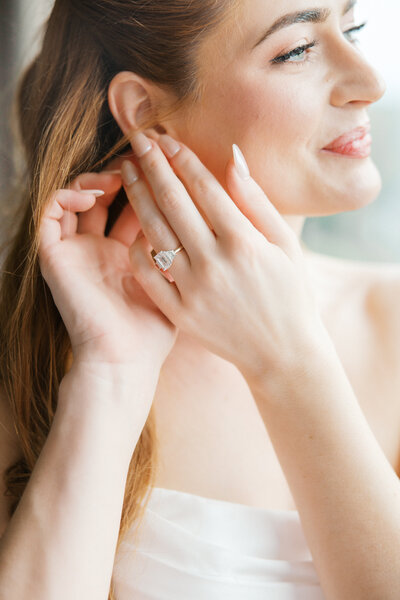 Red headed Bride with blue eyes touches earring in ear with her emerald cut diamond engagement ring on hand
