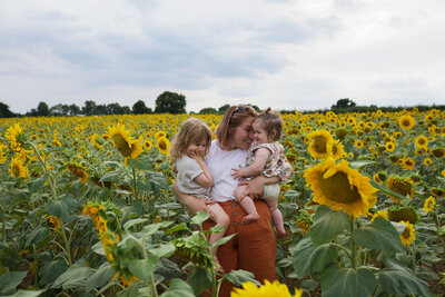 Mother standing in a field of sunflowers holding her two daughters on her hip