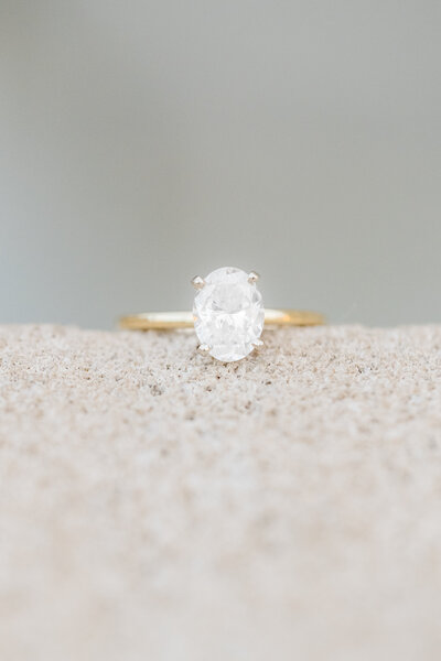 oval diamond in yellow gold ring sitting on cement step