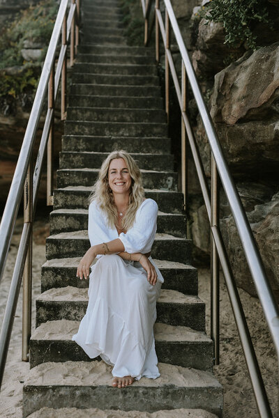 Woman dressed in white sitting at the base of an outdoor staircase