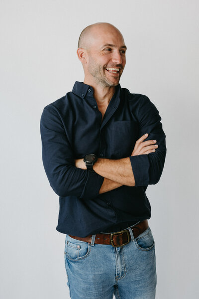A very minimal joyful headshot - a smartly dressed man laughs at the camera , he is against a white backdrop and is wearing a smart button up shirt