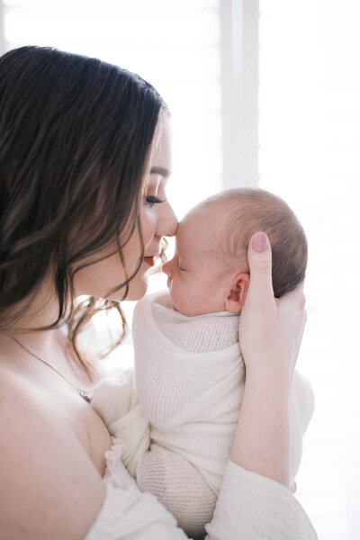 Newborn portrait taken in a studio in Jacksonville Beach with mom nuzzling her nose to baby’s nose by the window