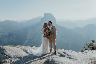 bride and groom running hand in hand down road with half dome in the background during their Yosemite elopement